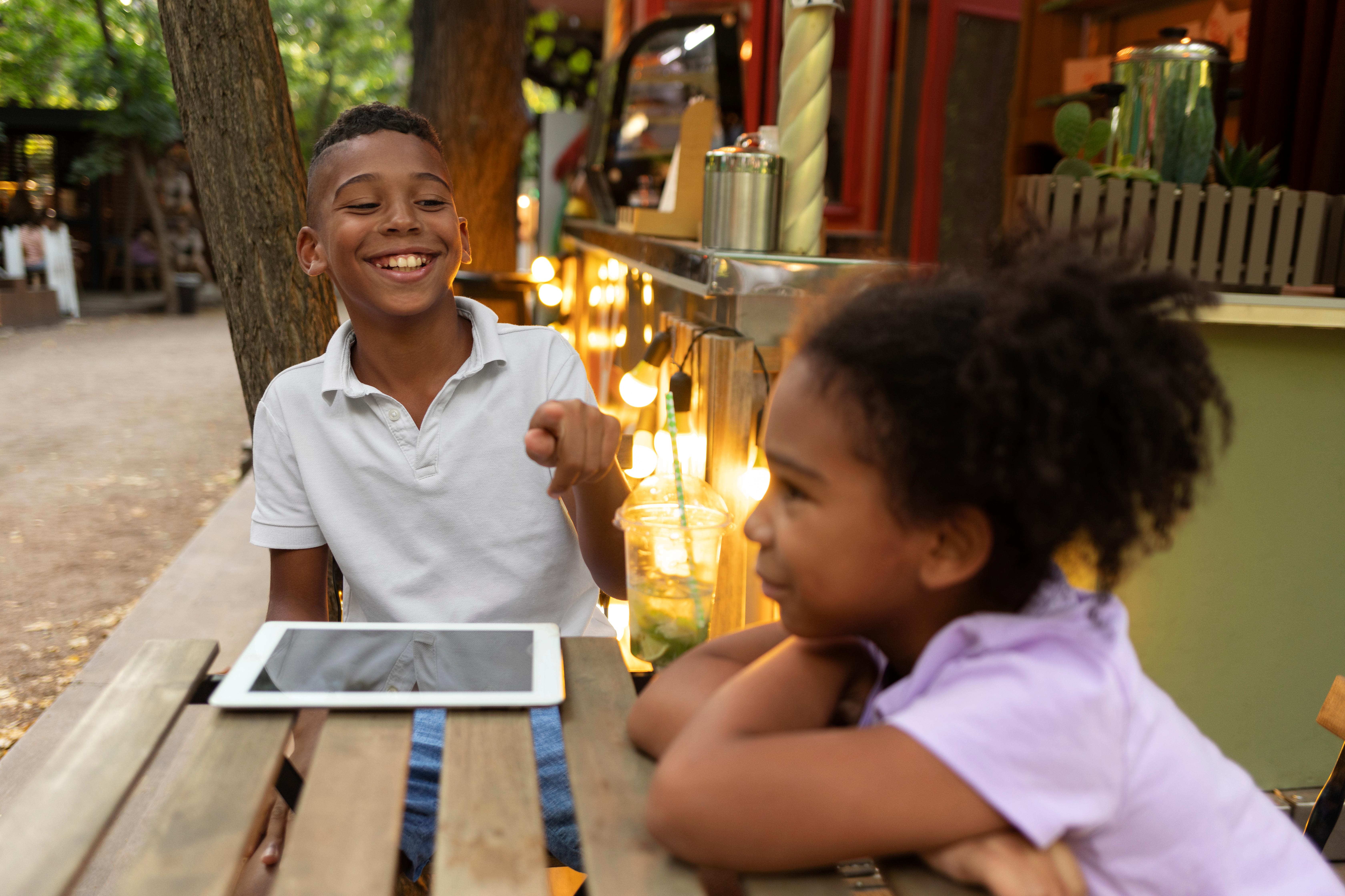Smiling children sitting at an outdoor table using a tablet, representing access to technology for students in Africa